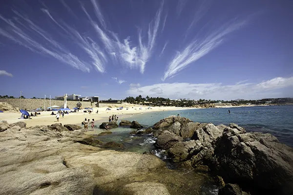 Chileno Bay beach in Los Cabos with clear blue water, rocky shoreline, and people enjoying a swimmable beach