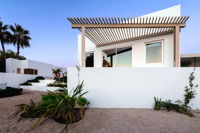 Modern white luxury villa exterior in Los Cabos with minimalist Baja architecture, pergola roof detail, and desert landscaping.