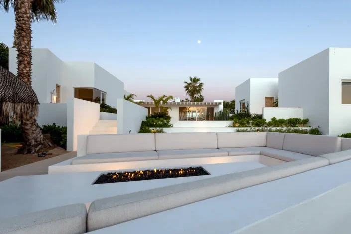 Modern luxury white villa courtyard in Los Cabos with minimalist architecture, outdoor fire feature, and soft evening light.
